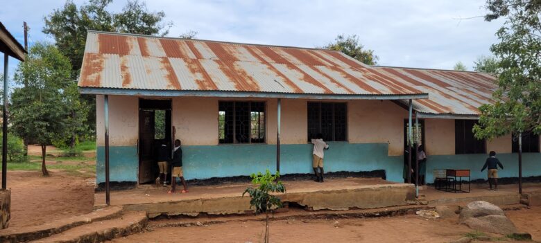 Kisegen peruskoulun rakennus, jonka luokkahuoneen ovella seisoo kaksi oppilasta. Kolmas oppilas kurkkii luokkahuoneeseen sisään ikkunasta.